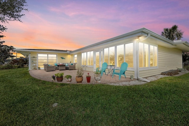 back house at dusk with an outdoor living space, a yard, and a patio area