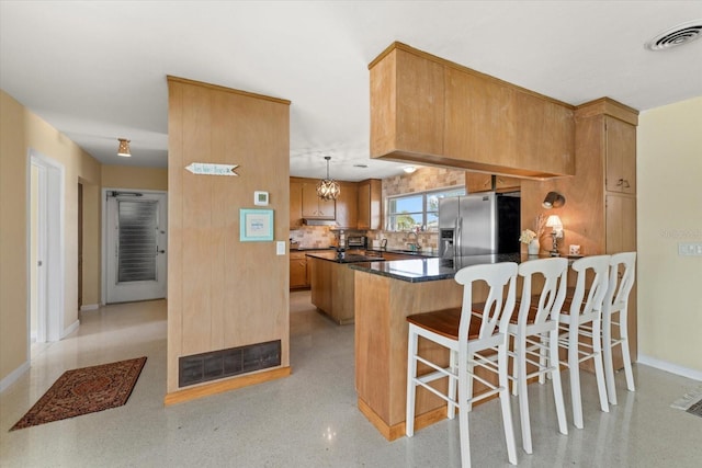 kitchen featuring a breakfast bar, stainless steel fridge with ice dispenser, kitchen peninsula, pendant lighting, and backsplash