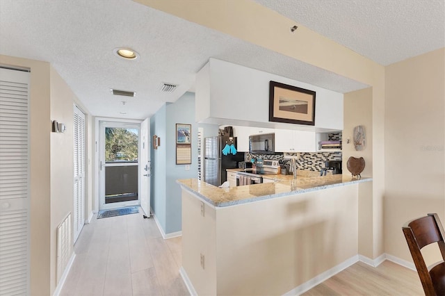 kitchen with light stone counters, appliances with stainless steel finishes, kitchen peninsula, white cabinets, and backsplash