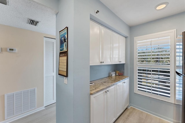 bar with white cabinetry, light stone countertops, and light hardwood / wood-style floors