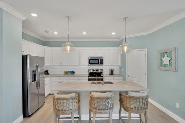 kitchen with pendant lighting, appliances with stainless steel finishes, white cabinetry, light stone countertops, and a center island with sink