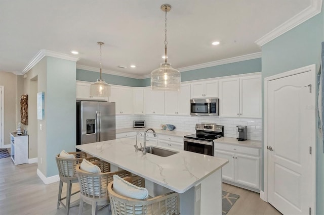 kitchen with appliances with stainless steel finishes, decorative light fixtures, white cabinetry, sink, and a center island with sink