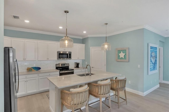 kitchen with stainless steel appliances, hanging light fixtures, a kitchen island with sink, and white cabinets