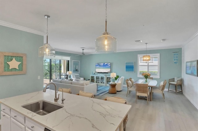 kitchen featuring sink, decorative light fixtures, light stone countertops, a kitchen island with sink, and white cabinets