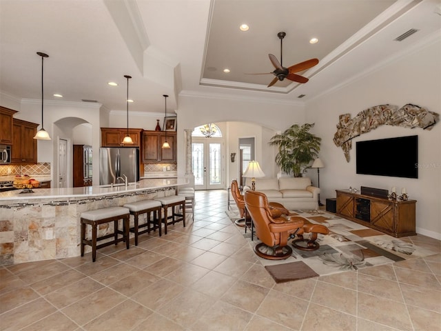 tiled living room featuring ornamental molding, a tray ceiling, ceiling fan, and french doors