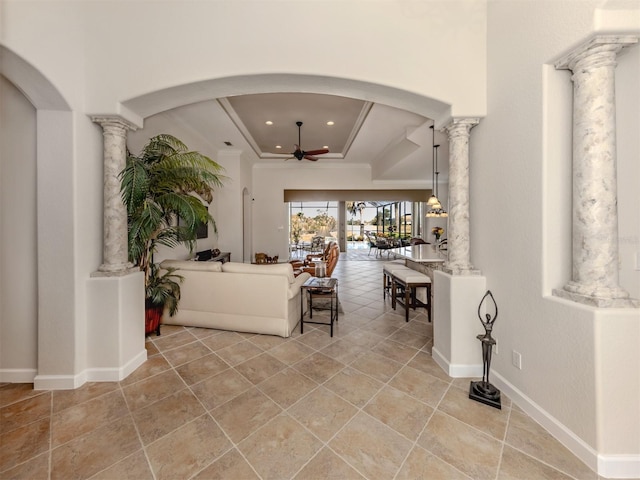 interior space featuring crown molding, ceiling fan, a tray ceiling, and decorative columns