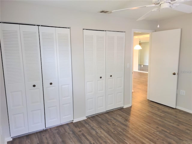 unfurnished bedroom featuring two closets, dark hardwood / wood-style floors, and ceiling fan