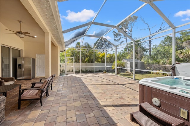 view of patio featuring a lanai, a hot tub, ceiling fan, and a storage unit