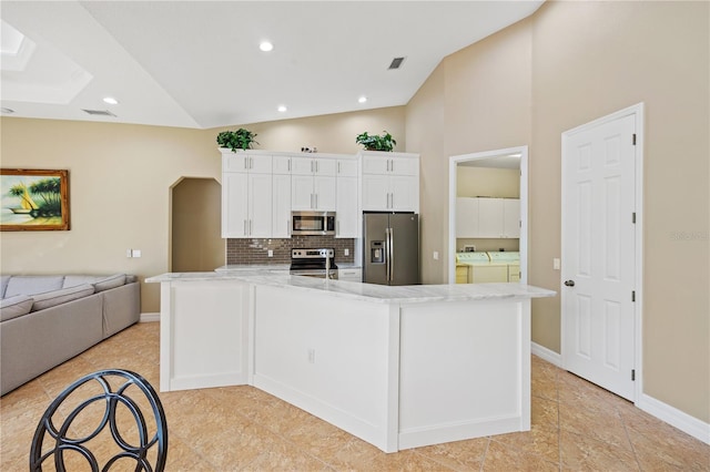 kitchen with stainless steel appliances, vaulted ceiling, white cabinets, separate washer and dryer, and decorative backsplash