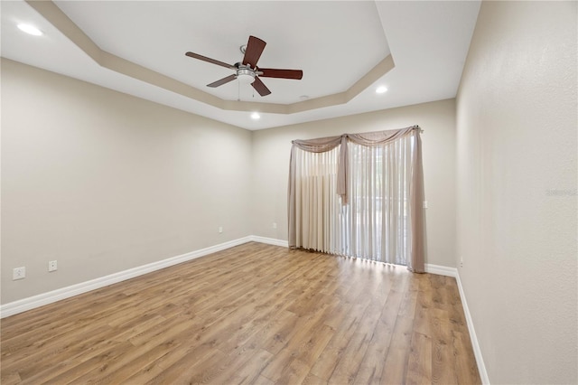 spare room with ceiling fan, a tray ceiling, and light wood-type flooring