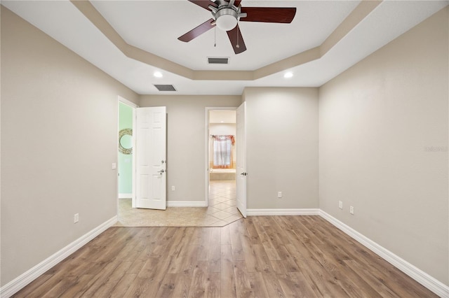 unfurnished room featuring ceiling fan, a tray ceiling, and light hardwood / wood-style flooring