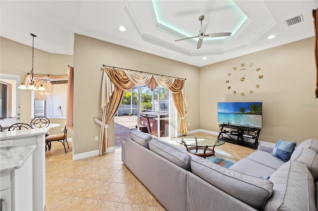 living room featuring light tile patterned flooring, a raised ceiling, and ceiling fan with notable chandelier