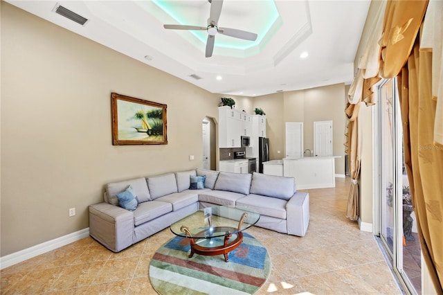 living room featuring a tray ceiling, sink, ceiling fan, and light tile patterned floors