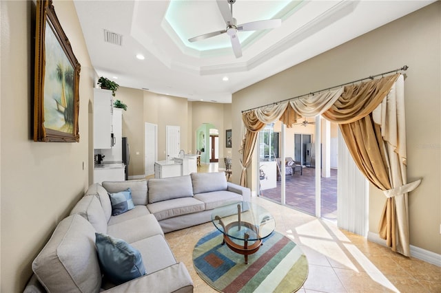 tiled living room with a raised ceiling, ceiling fan, and a towering ceiling