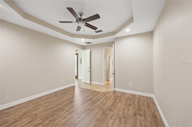 unfurnished room with a tray ceiling, ceiling fan, and light hardwood / wood-style flooring