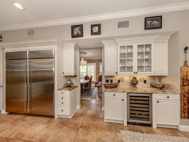 kitchen with backsplash, stainless steel built in refrigerator, light stone counters, white cabinets, and beverage cooler