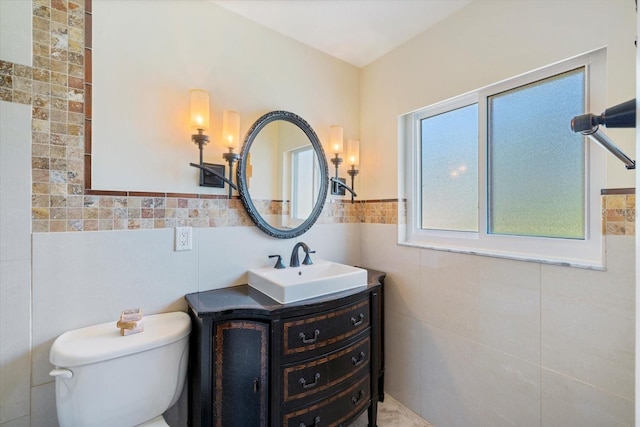 bathroom with a wainscoted wall, toilet, tile walls, and vanity