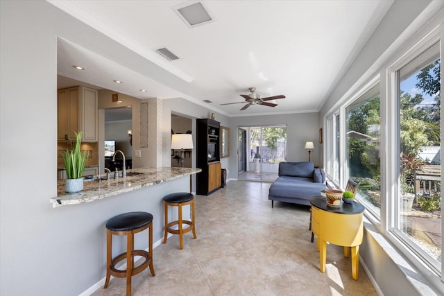 kitchen featuring visible vents, light stone counters, a kitchen breakfast bar, open floor plan, and crown molding