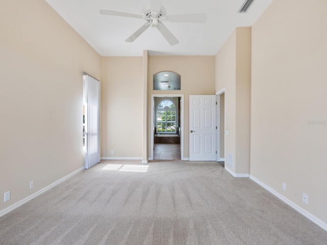 carpeted empty room with ceiling fan and a high ceiling