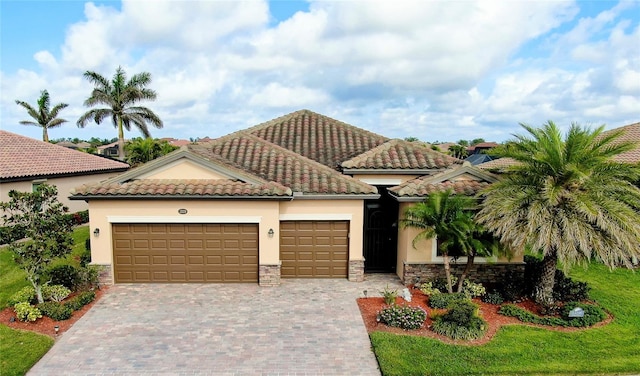 mediterranean / spanish home with stone siding, decorative driveway, an attached garage, and stucco siding