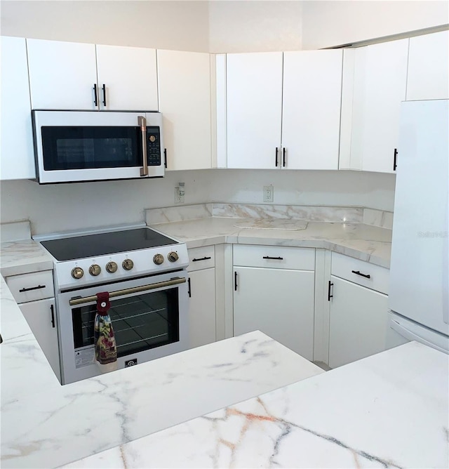 kitchen featuring white cabinets, light stone counters, and white appliances