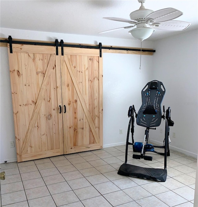 exercise area featuring light tile patterned flooring, a barn door, baseboards, and a ceiling fan