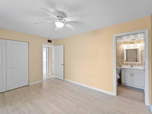 unfurnished bedroom with connected bathroom, sink, light wood-type flooring, a closet, and ceiling fan