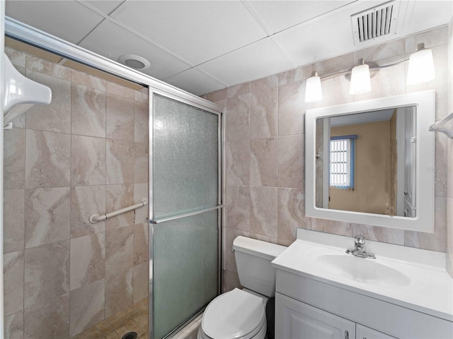 bathroom with tile walls, vanity, a shower with door, and toilet