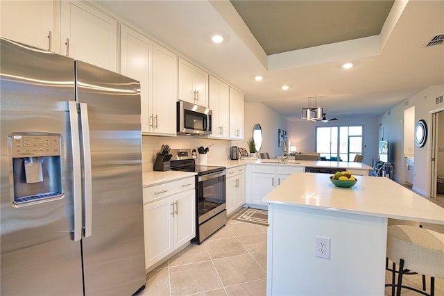 kitchen with light tile patterned floors, stainless steel appliances, recessed lighting, a raised ceiling, and a peninsula