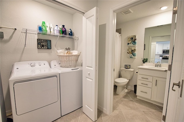 washroom featuring light tile patterned floors, laundry area, a sink, visible vents, and washing machine and clothes dryer