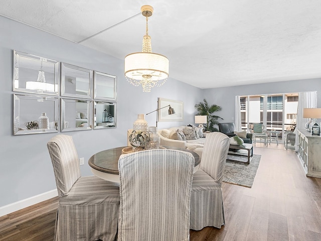 dining space featuring a chandelier, a textured ceiling, baseboards, and wood finished floors