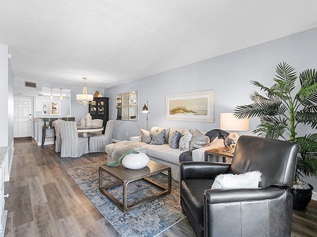 living room featuring wood finished floors, visible vents, and an inviting chandelier