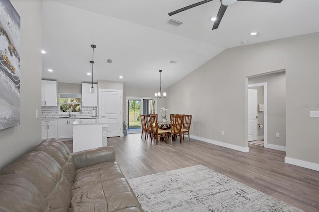 living room featuring sink, ceiling fan with notable chandelier, vaulted ceiling, and light hardwood / wood-style floors