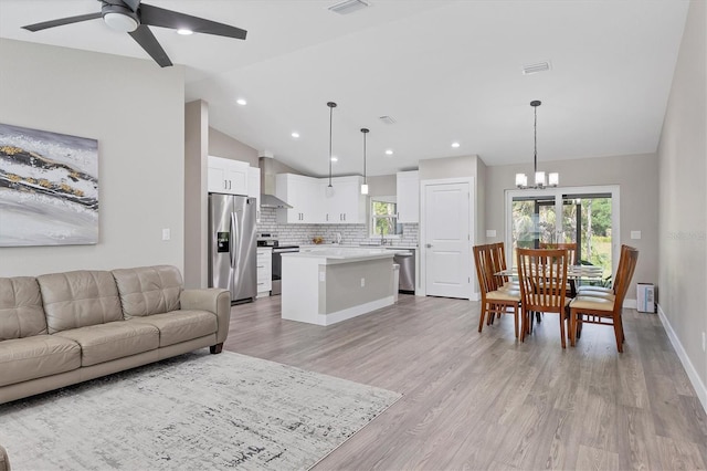 living room with vaulted ceiling, a healthy amount of sunlight, ceiling fan with notable chandelier, and light hardwood / wood-style floors