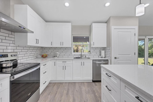 kitchen with decorative light fixtures, white cabinetry, sink, stainless steel appliances, and wall chimney range hood