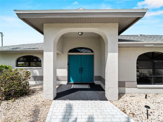 view of exterior entry with roof with shingles and stucco siding