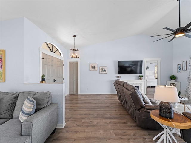 living room with vaulted ceiling, dark wood-type flooring, ceiling fan with notable chandelier, and baseboards