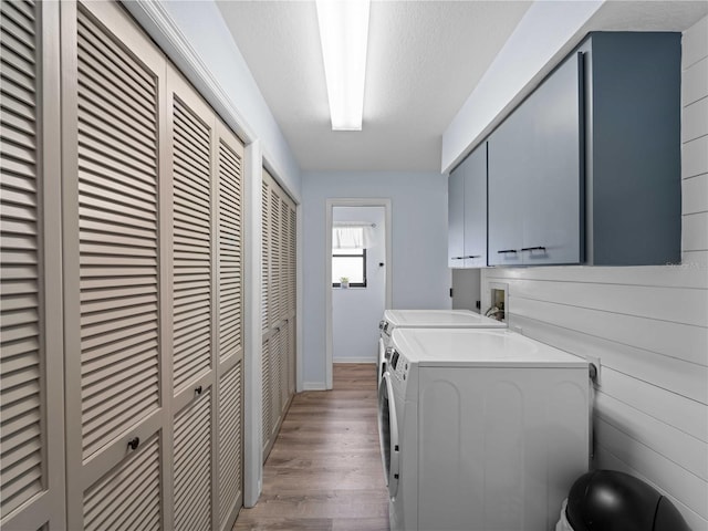 laundry area with light wood-type flooring, washer and dryer, cabinet space, and a textured ceiling