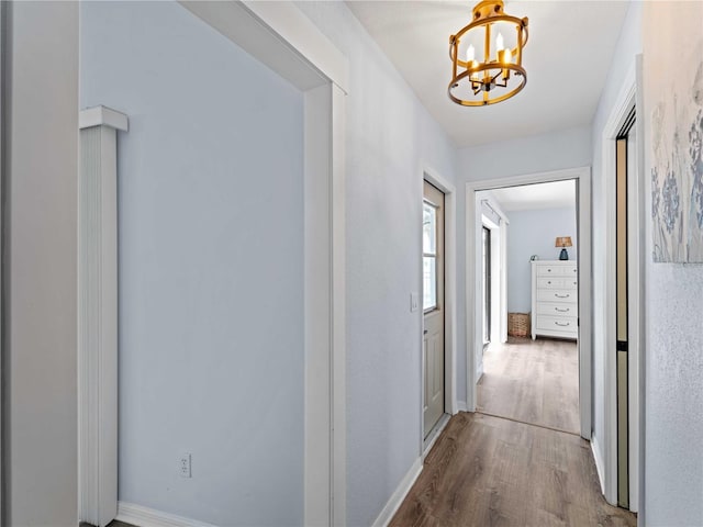 corridor featuring wood finished floors, baseboards, and an inviting chandelier