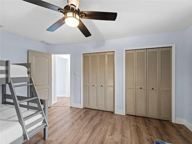 unfurnished bedroom featuring a ceiling fan, baseboards, multiple closets, and wood finished floors