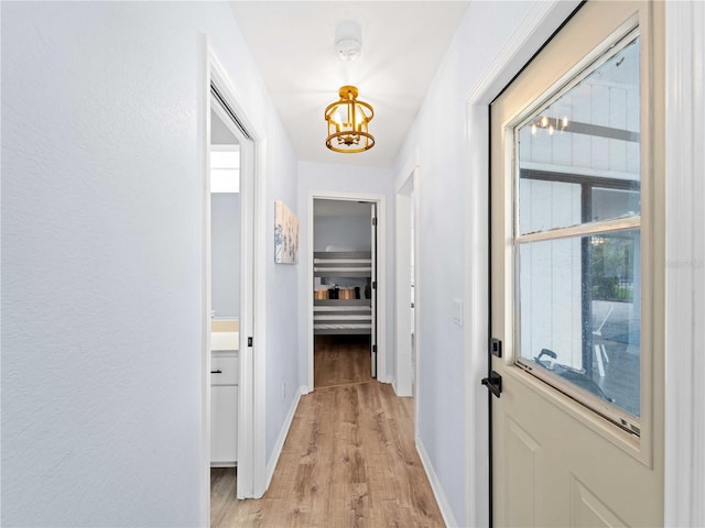 hall featuring baseboards, an inviting chandelier, and light wood-style floors