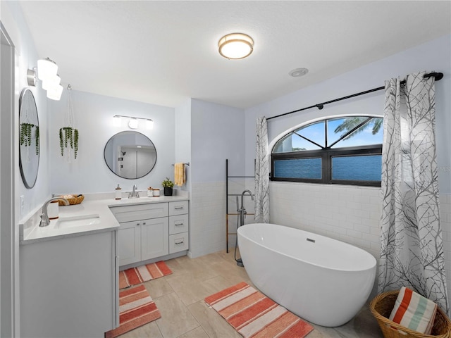 full bath featuring a wainscoted wall, tile walls, a freestanding bath, vanity, and tile patterned floors