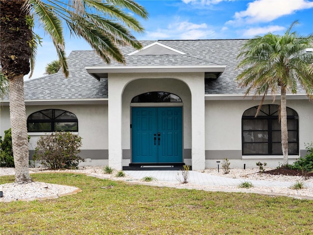 entrance to property with a yard, a shingled roof, and stucco siding