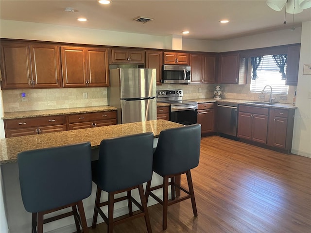 kitchen with light stone counters, appliances with stainless steel finishes, a kitchen breakfast bar, and sink