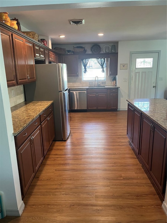 kitchen featuring dark brown cabinets, hardwood / wood-style flooring, stainless steel appliances, light stone countertops, and decorative backsplash