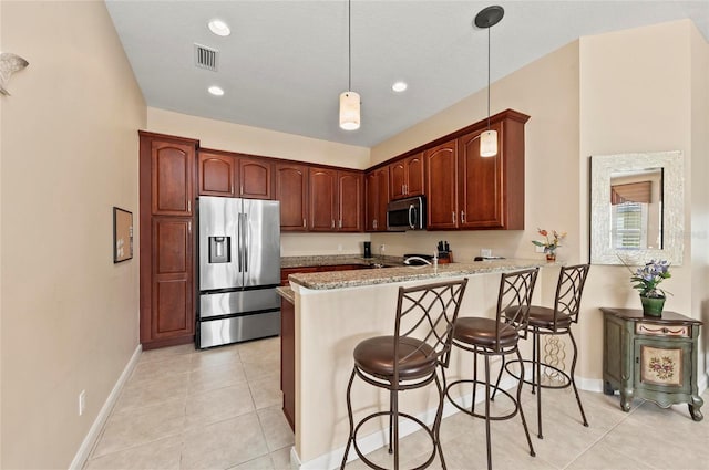 kitchen with appliances with stainless steel finishes, decorative light fixtures, a kitchen bar, kitchen peninsula, and light stone countertops