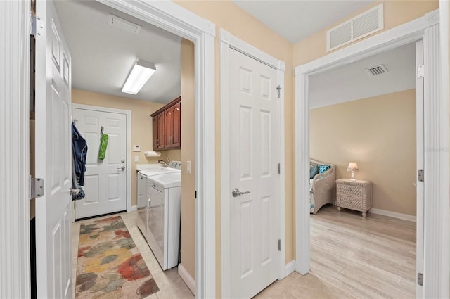 washroom with washing machine and dryer, cabinets, and light wood-type flooring