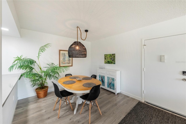 dining space featuring a textured ceiling, light wood-style flooring, and baseboards