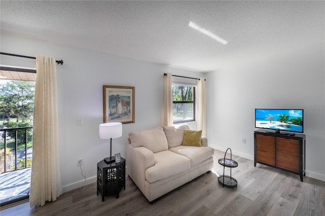 living area featuring a textured ceiling, light wood-style flooring, and baseboards