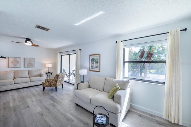 living area featuring light wood-type flooring, visible vents, ceiling fan, and a textured ceiling